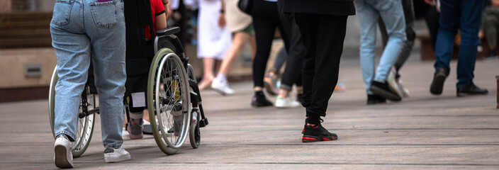 Woman walking on a crowded city street with her husband in a wheelchair, the lifestyle of a disabled person, stock photo