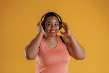 Front view, in headphones, listening to music. African American woman is in the studio against yellow background