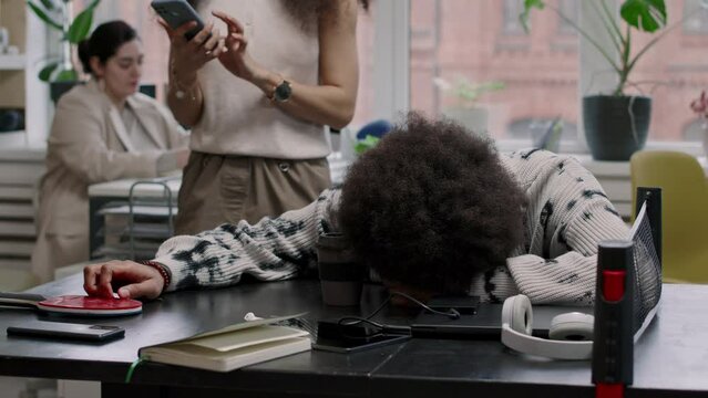 Medium shot of Biracial office employee napping on tennis table at workplace and his hilarious female colleague taking selfie portrait on smartphone with him while passing by