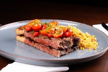 perfectly cooked sirloin steak with fat, cherry tomato salad and farofa at a steakhouse dinner, close-up