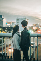 歩道橋から夜景を眺めるカップルの後ろ姿（縦写真）