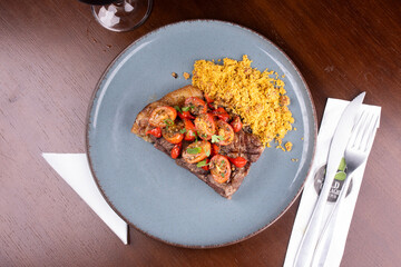 two pieces of sirloin steak cooked with fat cherry tomato salad and farofa at a steakhouse dinner...