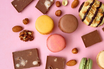 Pastel macarons, almond chocolate, peanut butter cookies and various nuts on bright pink background. Top view.