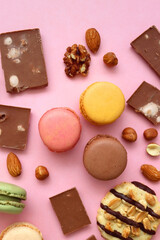 Pastel macarons, almond chocolate, peanut butter cookies and various nuts on bright pink background. Top view.