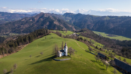 Aerial view of the famous place in Slovenia, the hilltop white church of Saint Thomas, surrounded by spectacular Drone view of Alps mountain range.