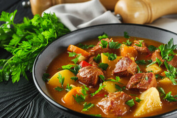 fragrant thick goulash soup on a black wooden rustic background