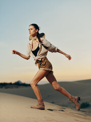 Woman running through desert sand dunes with hat and backpack, enjoying outdoor adventure and freedom