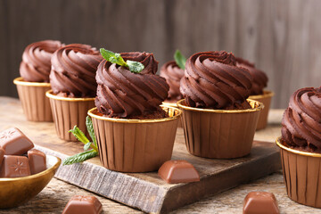 Delicious cupcakes with chocolate pieces and mint on wooden table