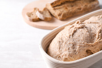 Fresh sourdough in proofing basket on light table, closeup. Space for text