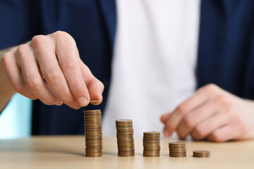 Financial savings. Man stacking coins at wooden table, closeup