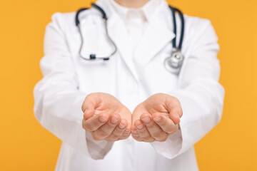 Doctor with stethoscope holding something on orange background, closeup