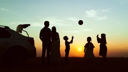Silhouettes children parents at sunset near car in field. Family vacation in nature road trip...