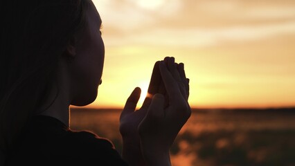 Woman praying with folded hands at sunset silhouette. Religious pious orthodox christian spiritual...