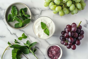 Ingredients for a grape smoothie laid out on a marble countertop, including fresh grapes, yogurt, and mint leaves