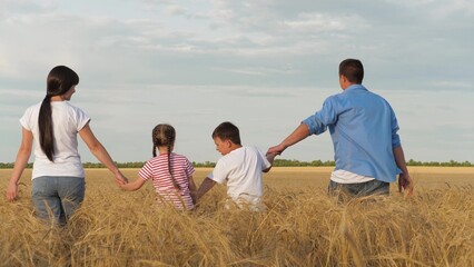 Mother father and kids walking at dry wheat field holding hands relaxing outdoor back view. Happy family going agriculture cereal harvest plantation organic nature landscape freedom leisure activity