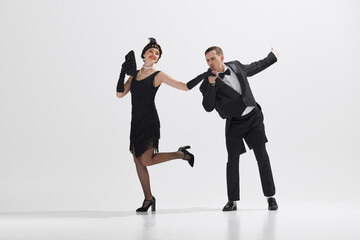 Young couple styled in 1920s fashion, elegant man and woman dancing isolated against white studio...