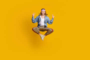 Full size photo of cool young man show v-sign jump empty space wear denim shirt isolated on yellow...