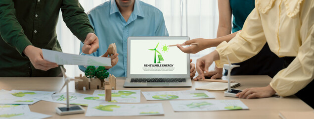 Renewable energy logo displayed on green business laptop while business team represented green...