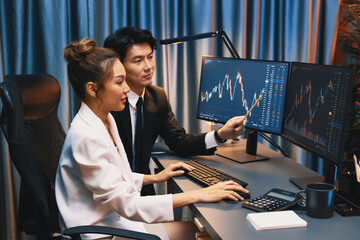 Smiling Asian business traders pointing to dynamic stock exchange data screen profit value online...