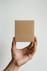 Hand holding a square brown paper box in front of beige background