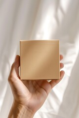 Hand holding a square brown paper box in front of beige background