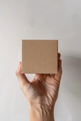 Hand holding a square brown paper box in front of beige background