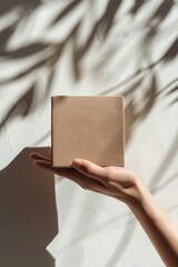 Hand holding a square brown paper box in front of beige background