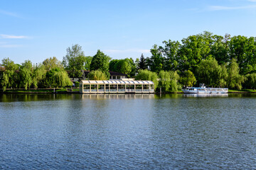 Landscape with white boats on Herastrau lake and large green trees in King Michael I Park (former Herastrau) in Bucharest, Romania, in a sunny autumn day.