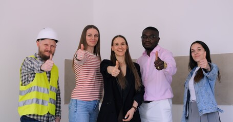Fototapeta premium Diverse company professionals give thumbs-up in renovation setting. Company unity shown by builders, architects, designers. Optimistic company workforce, multiethnic, modern renovation scene.