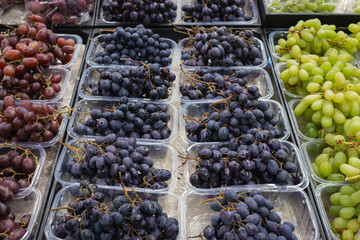 Variety of grapes on market stall. Different sorts of grapes in basket. Heap of black, pink and...
