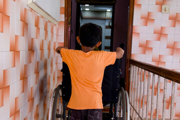 Asian boy moving wheelchair standing at the door of home
