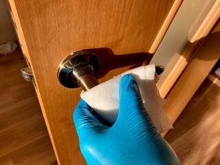 Person in blue gloves cleans wood door handle with cloth