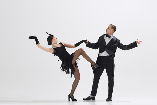 Stylish couple reenacts 1920s dance, woman in fringe dress and man in dapper black suit dancing isolated over white studio background. Concept of art, retro and vintage, hobby, entertainment, 20s