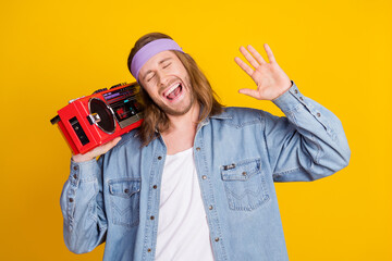Portrait of cool young man carry boombox wear denim shirt isolated on yellow color background