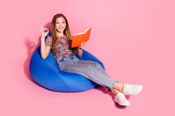 Full length photo of lovely teen lady sit bean bag read book show okey dressed stylish print...