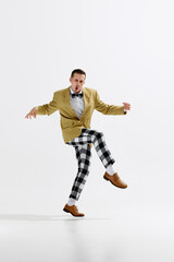 Stylish young man in dynamic pose wearing checkered trousers and mustard jacket, emotionally dancing isolated over white studio background. Concept of art, retro and vintage, hobby, entertainment, 20s