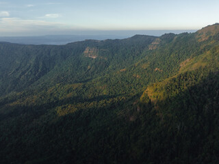 Obraz premium The fading light of dusk gently touches the slopes of a mountain blanketed with dense greenery, hinting at the vast wilderness.