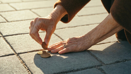 Close-up, hand of elderly woman lifting coin from pavement tiles on street, concept of old age and poverty, Film grain effect