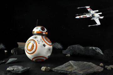 Naklejka premium a droid robot character in the Star Wars movie name BB-8 (or Beebee-Ate) display on stone table with background of X-wing Starfighter in black space many stars wall in the star war movie toy shop