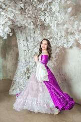 Beautiful smiling woman in fantasy white and purple rococo style medieval dress dancing near tree with white flowers