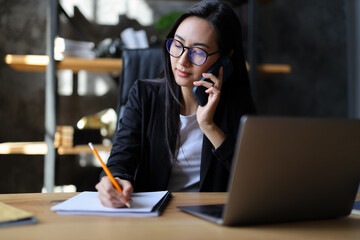 A young Asian businesswoman sitting at her desk, using a computer, talking on the phone...