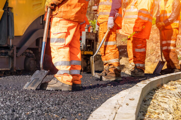 roadworkers in hi-viz laying hot tarmac new road surface on residential housing development site 