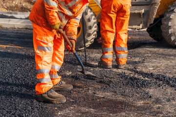 roadworkers with shovels in hi-viz laying hot tarmac new road surface on building site 