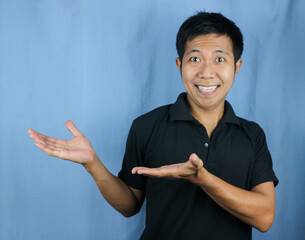 Portrait of young Asian man smiling with open palm gesture advertising and product placement concept