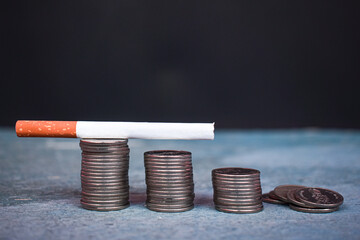 A lit cigarette was slowly being extinguished, placed on top of a pile of coins. Cigarette concept.
