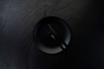 Black plate with fork and knife on dark table