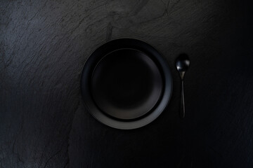 Minimalist black soup plate with spoon on black slate slab