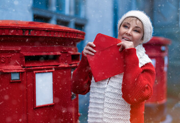 woman sending celebrate envelope to red postbox on snowy day before Christmas