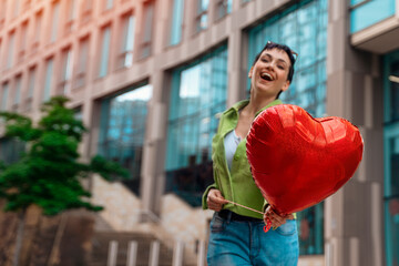 joyful woman with heart-shaped balloon falling in love walking around city. Lifestyle people  