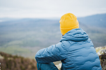 a man in a blue jacket and yellow hat is sitting on top of a mountain